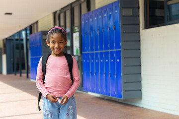 young girl smiling in school hallway near bright blue lockers, carrying black backpack