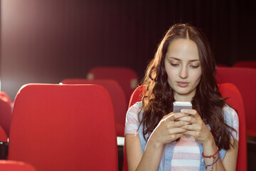 bi-racial young adult woman sitting alone in red auditorium seats using smartphone, copy space