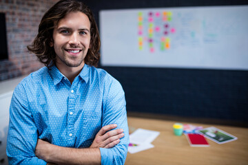 Man standing crossing arms and smiling in modern office, with whiteboard and coffee cup