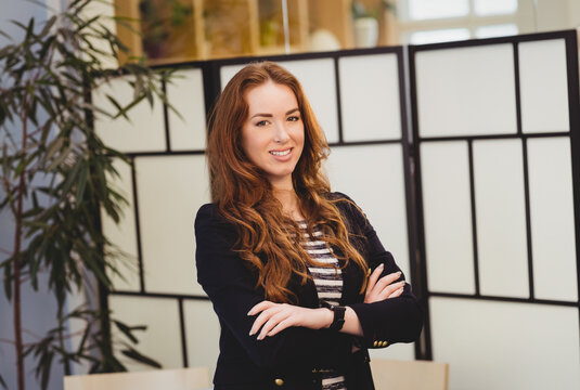 Woman standing confidently in office space, with smartwatch, glass divider and bamboo plant