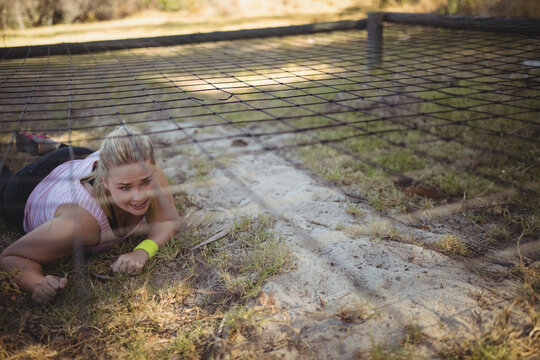 Woman crawling under low mesh net in outdoor obstacle course, wearing neon wristband, copy space