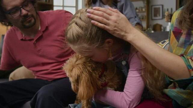 Medium shot of happy, excited Caucasian father with disability, mother, teenage son and daughter sitting on couch together, cuddling with new pet maltipoo dog adopted from shelter and giving it treats