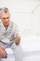 Senior man examining medical inhaler device on bed in clinical bedroom, reflecting health routine