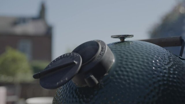 A grill with a lid on top of it. The lid has a knob on it. The grill is green