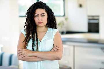 Young woman standing with arms crossed in open-plan home interior, with sofa and kitchen countertop