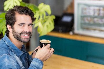 Male barista holding ceramic coffee cup and saucer at café counter with pastry display, copy space