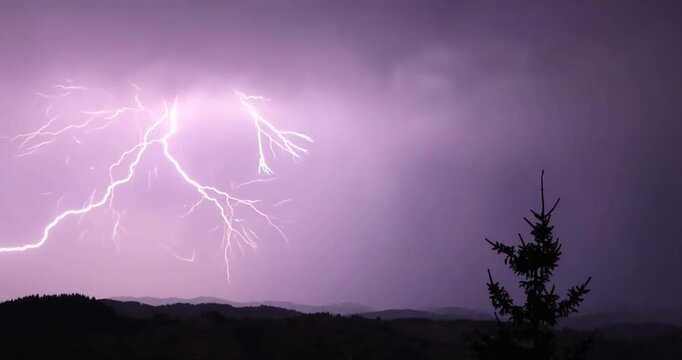 Lightning storm in the night sky at mountain. Multiple lightnings and thunders illuminate night sky and hills with firs