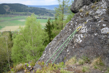 Mountaineering safety rope and anchor installed on rock face. Spring scenery with trees and valley perfect for outdoor activity themes and extreme sports visuals.