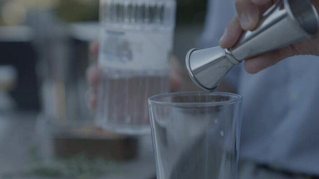 A man is pouring a clear liquid into a glass. The liquid is likely a type of alcohol, such as vodka or gin. The man is using a small silver device, possibly a shot glass or a cocktail shaker