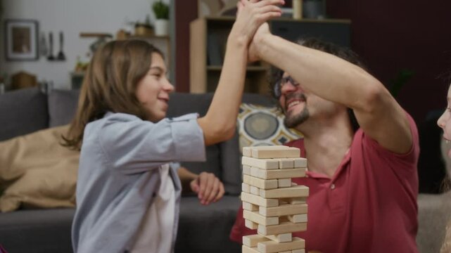 Medium shot of happy Caucasian father with limb difference disability and children playing wooden blocks game, boy successfully removing difficult piece, dad cheering and giving high five