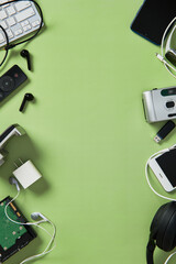 Flat lay of various electronic gadgets like keyboard, phone, headphones on green background....