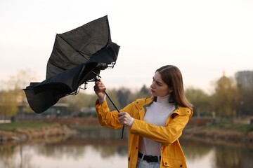 Teenage girl with broken umbrella fighting wind under rain outdoors