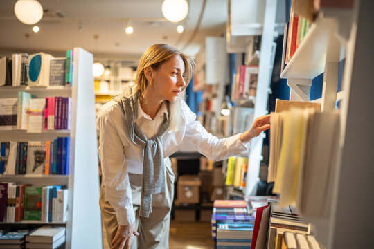 Enthusiastic woman selects books in bookstore alone. Female book lover browsing, searching textbooks, handbooks, library visit, book fair, book crossing, literature passion, bibliophile in store