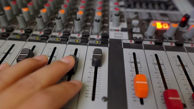 Hand of professional audio engineer operating mixing board faders in music recording studio, adjusting volume and equalizing sound during post production process
