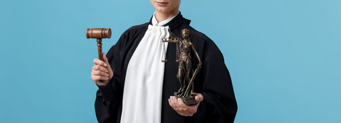 Judge with mallet and figure of Lady Justice on light blue background, closeup
