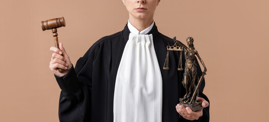 Judge with mallet and figure of Lady Justice on light brown background, closeup