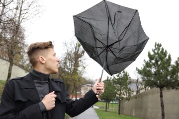 Man with broken umbrella fighting wind under rain outdoors