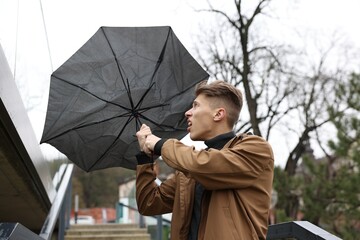 Man with broken umbrella fighting wind under rain outdoors