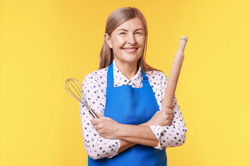 Happy woman with rolling pin and whisk on yellow background