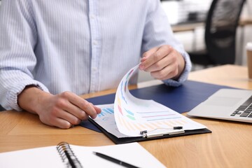 Man with papers working at wooden desk in office, closeup