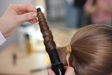 Hairdresser curling girl's hair in salon, closeup