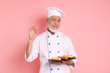 Professional pastry chef with delicious eclairs showing ok gesture on pink background