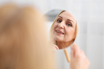 Smiling middle aged woman with round mirror on blurred background