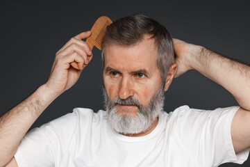 Obraz premium Handsome man combing his hair on dark grey background
