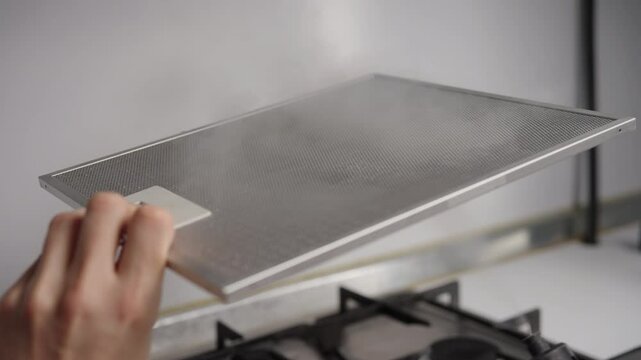 Professional cleaning worker wiping greasy extractor hood filter, removing accumulated grime with steam cleaning device, ensuring kitchen sanitation and spotless surface, close-up, slow motion.