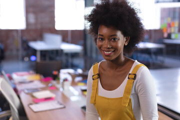 Young African American woman leaning on wooden table in office, with mug, sticky notes, copy space