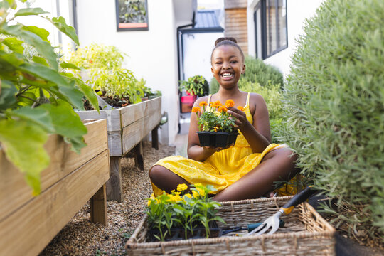 African American child girl sitting on gravel path near planter beds in backyard, holding seed tray