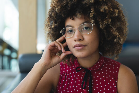 bi-racial woman resting head on hand while gazing at camera in cafe, with wire-frame eyeglasses