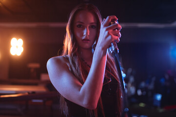 Woman in her twenties standing on club stage holding microphone, with amber and blue spotlights