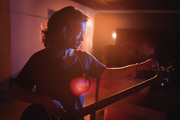 Japanese baby boy holding acoustic guitar neck in indoor dim room, showcasing warm stage lighting