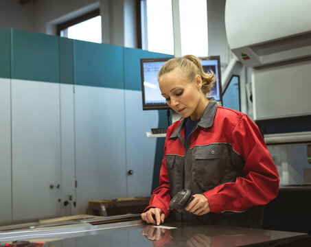 Woman scanning flat sheet with handheld scanner while viewing monitor on factory floor, copy space