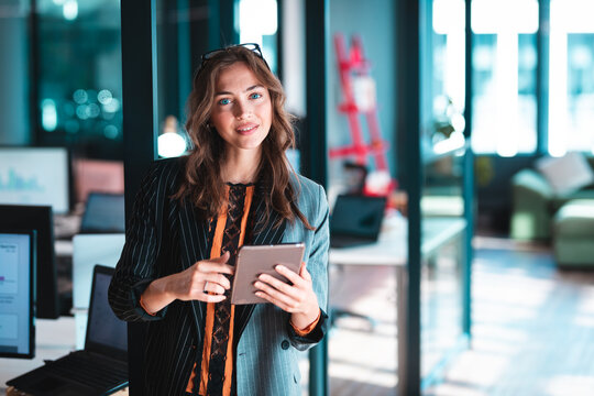 Young adult woman reviewing tablet in open?plan office with laptops stepladder and sofa