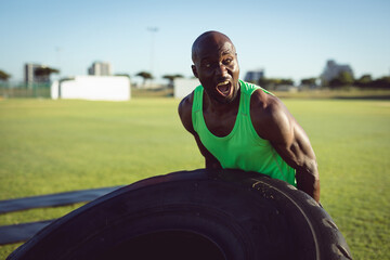 African American man flipping large tractor tire on grassy field, demonstrating strength training