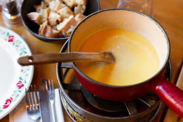 French variation of Swiss dish fondue, Fondue Savoyarde, preparing on table.