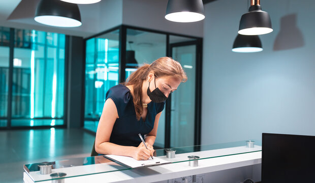 Woman signing register book on glass topped reception desk at office lobby, using pen