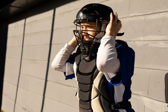 Female baseball catcher adjusting catchers helmet by concrete wall in sports dugout, copy space - Powered by Adobe