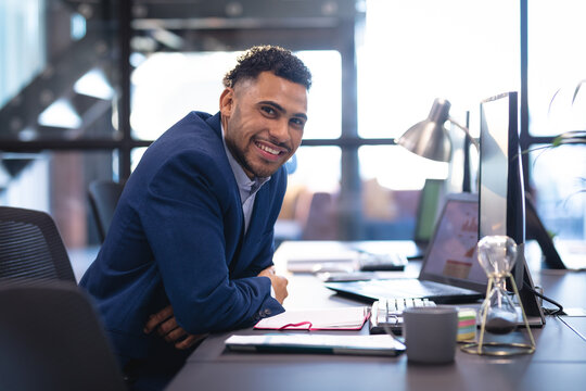 Businessman leaning forward on desk in modern office, showing laptop hourglass and coffee mug