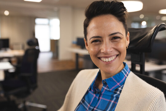 Woman sitting in ergonomic chair in modern open?plan office, smiling among desks and monitors