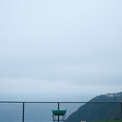 Fototapeta premium Green disc golf basket overlooks coastal hills on an overcast day; ideal for sports, leisure, or travel websites