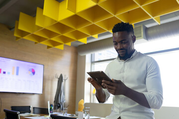 Mid adult African American man using tablet in meeting room with chart display, copy space