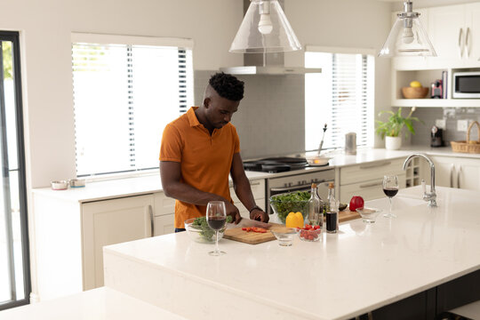 African American man slicing tomatoes in modern kitchen on wooden cutting board, with kitchen knife - Powered by Adobe