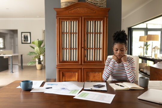 Woman using calculator and reviewing charts on wooden table in home workspace, copy space