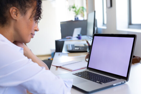 Woman leaning forward at desk in bright office, using laptop with notebook and pen, copy space