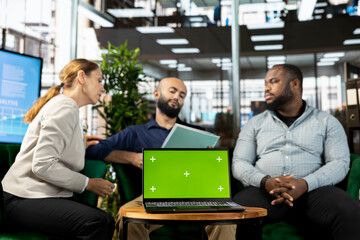 Green screen laptop in front of businesspeople talking in startup company, looking at financial business documents. Chroma key notebook used by diverse team of office clerks