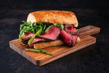 Traditional sliced cold cuts roast beef sandwich with rucola served as close-up on a wooden cutting board