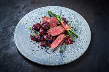 Traditionally roasted fillet of saddle of venison with chestnuts, bacon-wrapped bean sticks and redcurrants served with lingonberry sauce as close-up in a bowl with a rustic background